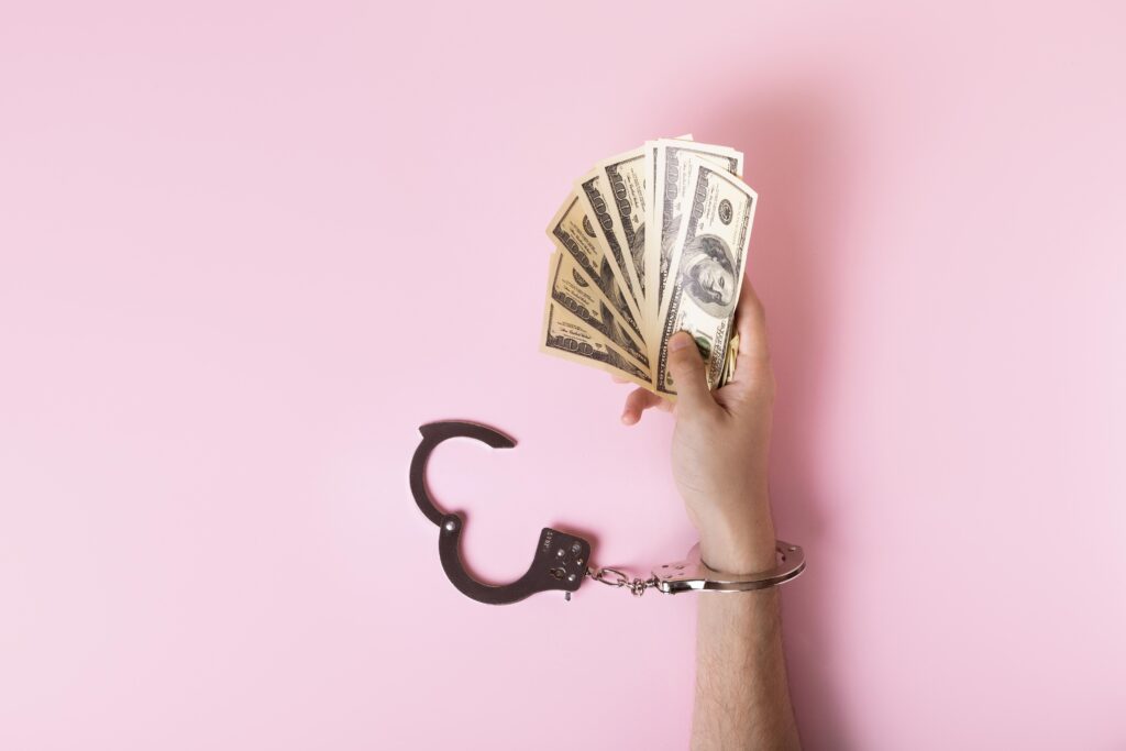 A financially independent hand, tied with open handcuff, is holding cash.